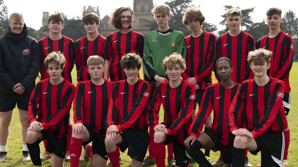 Eine Gruppe von jungen Fußballspielern steht auf dem Sportplatz der Westonbirt School mit einem Kirchturm im Hintergrund.
