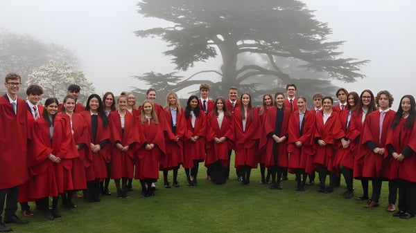 Eine große Gruppe von Schülerinnen und Schülern der Westonbirt School steht im roten Gewand auf einer Wiese vor einem großen Baum.
