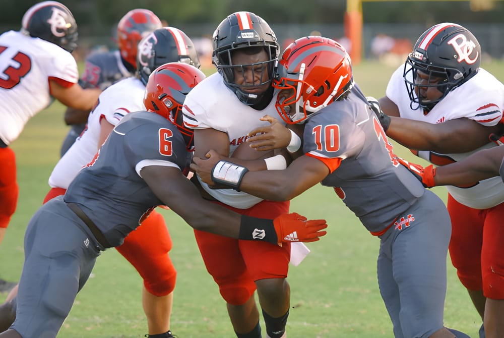 Schüler des Westside Secondary School spielen American Football auf einem grünen Spielfeld unter bewölktem Himmel.