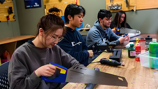 Eine Gruppe von Schülerinnen und Schülern der Westsyde Secondary School arbeitet gemeinsam an einem Tisch mit Laptops und elektronischen Geräten.