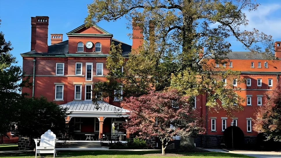 Das historische Backsteingebäude der Westtown School mit einem Turm steht umgeben von herbstlich gefärbten Bäumen unter klarem blauem Himmel.