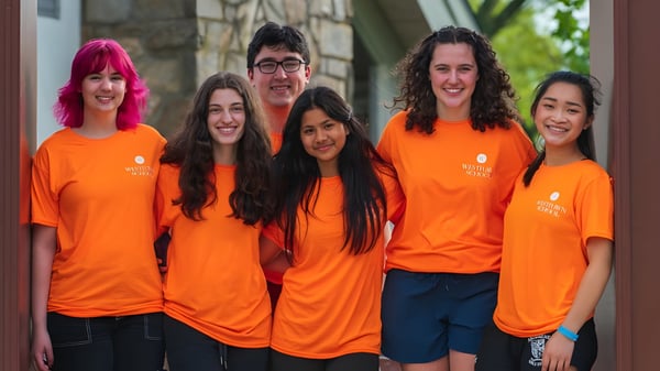 Eine Gruppe von Schülerinnen und Schülern der Westtown School trägt orange T-Shirts vor einem Steingebäude mit Grünflächen.
