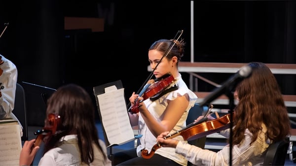 Eine Schülerin der Westtown School spielt Geige auf der Bühne umgeben von anderen Musikern.
