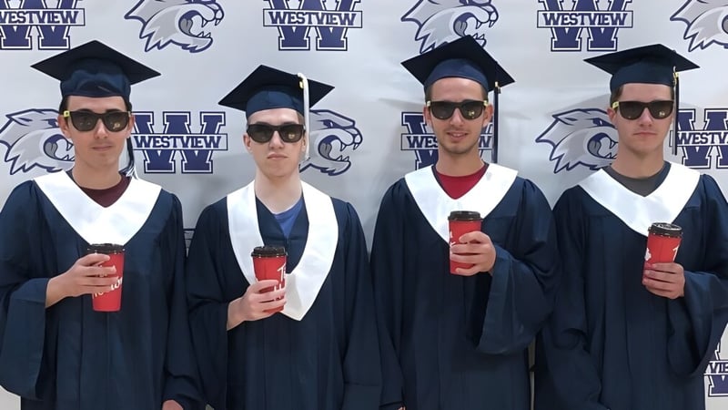 Vier Absolventinnen und Absolventen in akademischer Kleidung stehen vor einem Hintergrund mit dem Westview Secondary School Logo und Maskottchen.