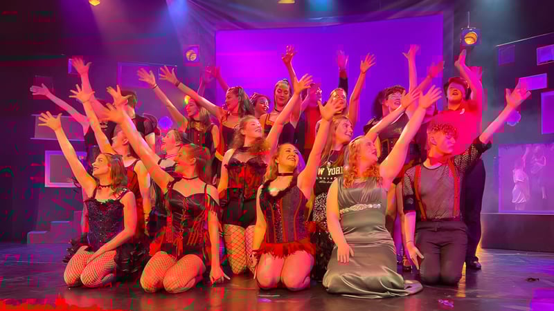 Schüler des Weymouth College führen auf der Bühne eine Aufführung mit erhobenen Armen und bunter Beleuchtung durch.