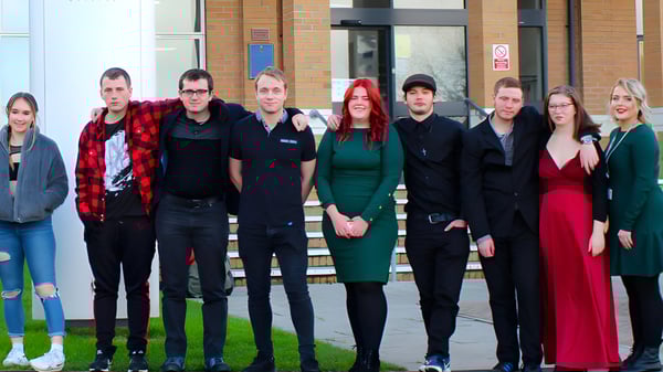 Eine Gruppe von Schülerinnen und Schülern steht vor dem Gebäude mit Glasfassade auf dem Campus des Weymouth College.