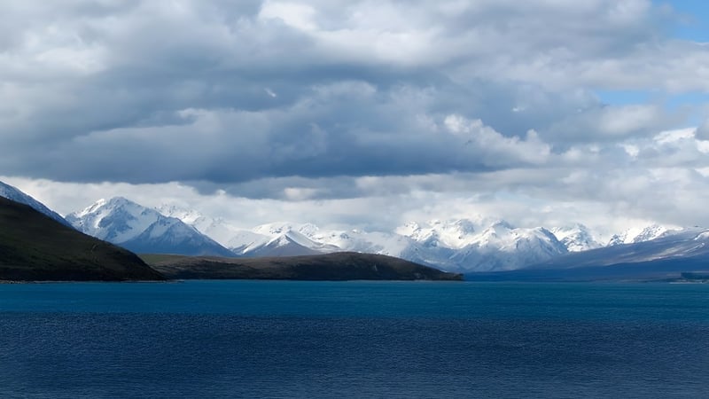 Ein See mit schneebedeckten Bergen und bewölktem Himmel, im Umfeld der Whakatane High School.