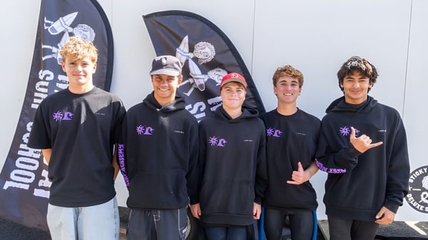 Eine Gruppe Schülerinnen und Schüler der Whangamata Area School trägt schwarze Hoodies vor einer Totenkopf-Leinwand.