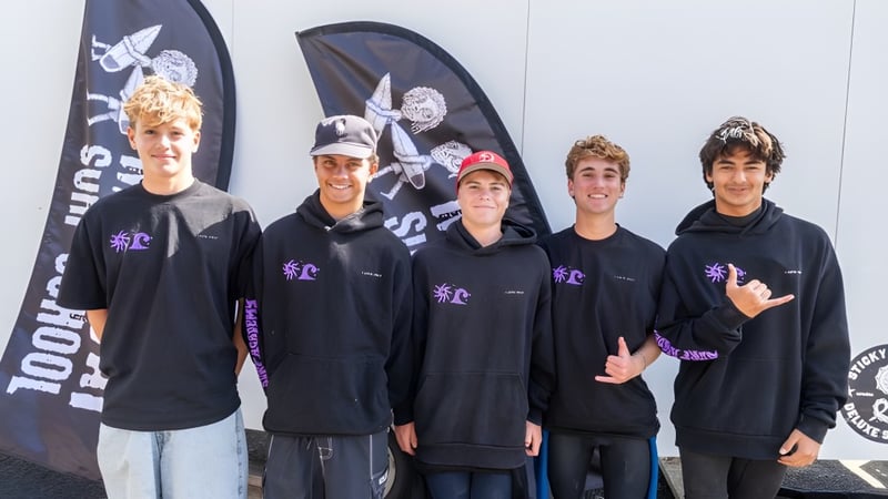 Eine Gruppe Schülerinnen und Schüler der Whangamata Area School trägt schwarze Hoodies vor einer Totenkopf-Leinwand.