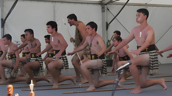 Eine Gruppe von Männern in traditioneller Kleidung führt auf der Bühne einen synchronen Tanz auf dem Campus der Whangamata Area School auf.