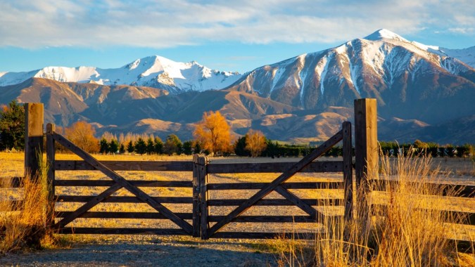 Ein rustikales Holztor mit Blick auf schneebedeckte Berge und herbstlich gefärbte Bäume auf dem Gelände der Whanganui Collegiate School.