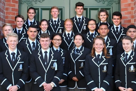 Eine Gruppe von Schülern der Whanganui Collegiate School steht in schwarzen Uniformen vor einem Backsteingebäude mit dekorativen Architekturdetails.