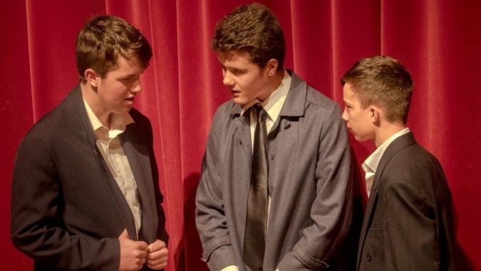 Drei Schüler der Whanganui Collegiate School in formeller Kleidung unterhalten sich vor einem roten Vorhang.