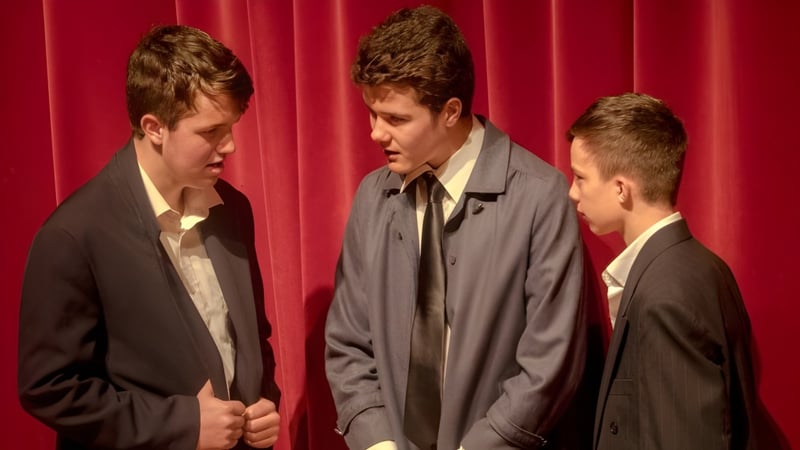 Drei Schüler der Whanganui Collegiate School stehen in formeller Kleidung vor einem roten Vorhang.