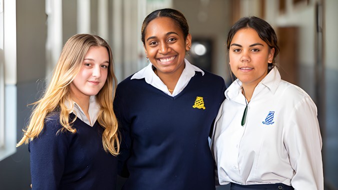 Drei Schülerinnen stehen im Flur des Whanganui Girls’ College und lächeln in die Kamera.