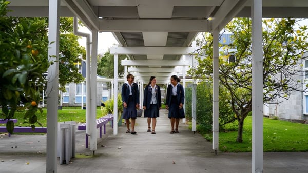 Schülerinnen in formeller Kleidung gehen auf einem überdachten Weg auf dem Campus der Whanganui Girls’ College, umgeben von Grünflächen und Bäumen.