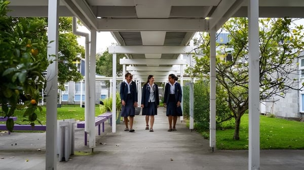 Schülerinnen und Schüler in formeller Kleidung gehen auf einem überdachten Weg umgeben von grünen Bäumen auf dem Campus der Whanganui Girls’ College.