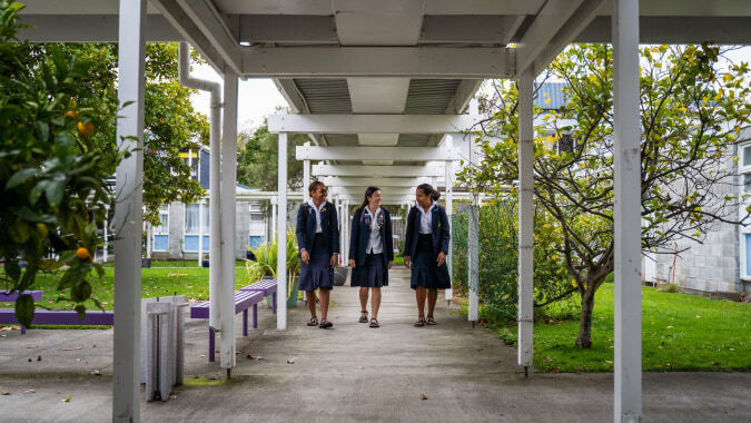 Eine Gruppe Schülerinnen in formeller Kleidung steht auf dem überdachten Weg am Whanganui Girls’ College, umgeben von grünen Bäumen.