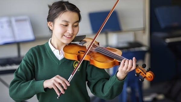 Eine Schülerin der Whanganui High School spielt Violine vor Musikinstrumenten im Hintergrund.