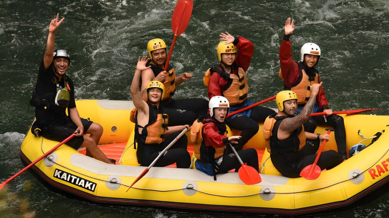 Schüler des Whangaparāoa College sitzen mit Schwimmwesten und Helmen in einem gelben Schlauchboot in einer bewaldeten Landschaft.