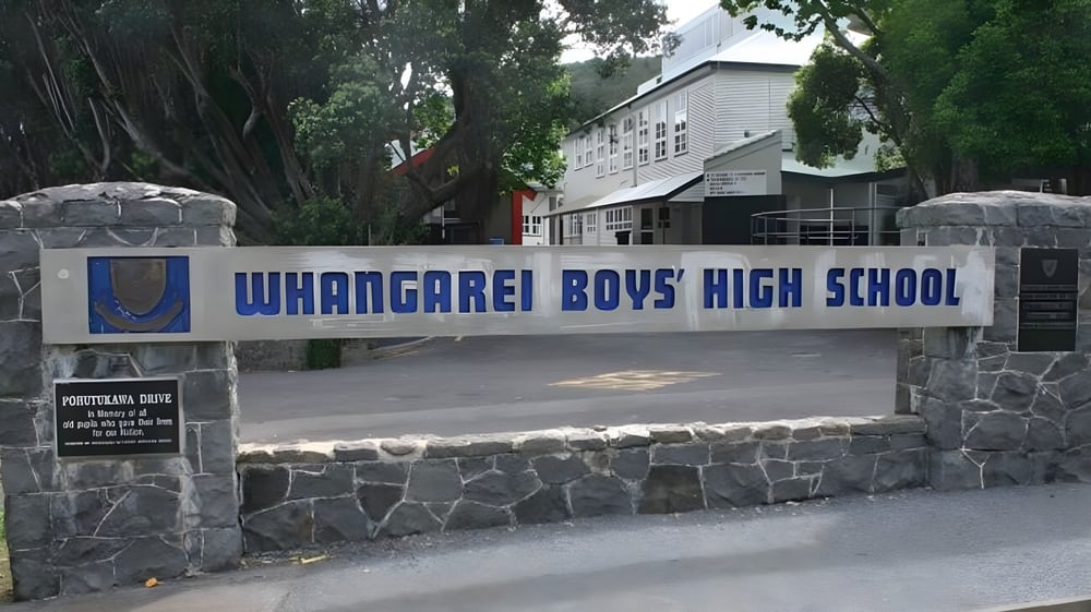 Der Eingang von Whangarei Boys’ High School mit Steinmauer, Schild und einem Gebäude im Hintergrund umgeben von Grünflächen.