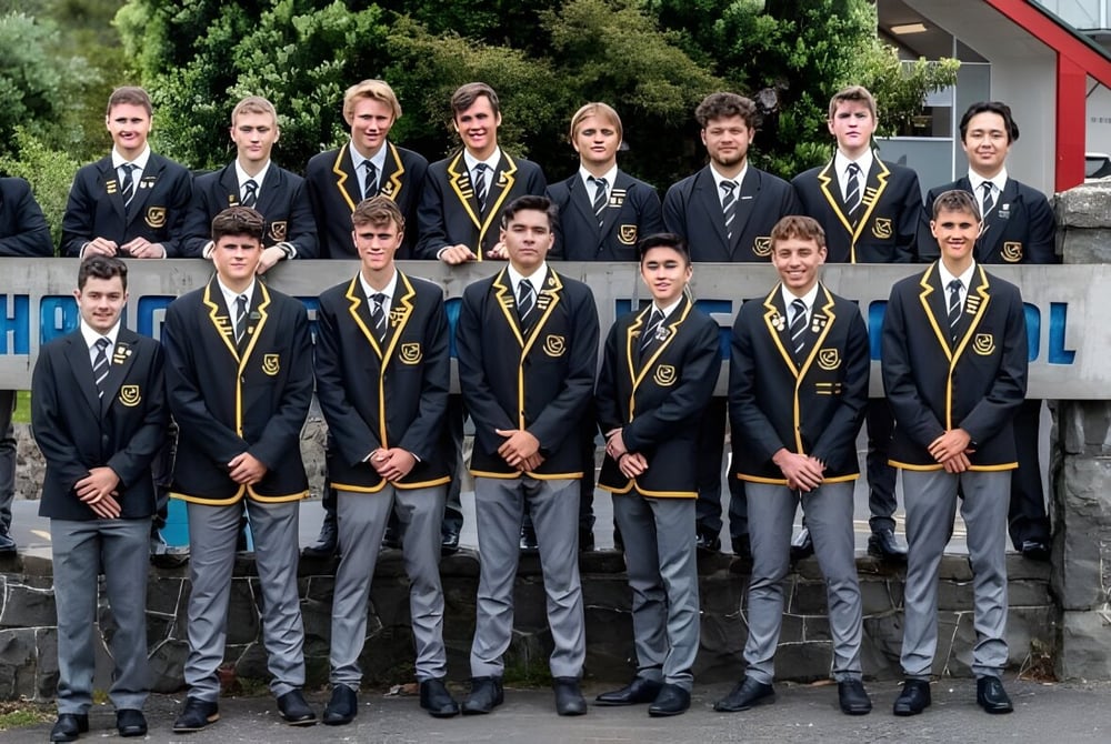 Eine Gruppe von Schülern der Whangarei Boys’ High School posiert vor dem Schulgebäude mit dem WHSPL-Schild.
