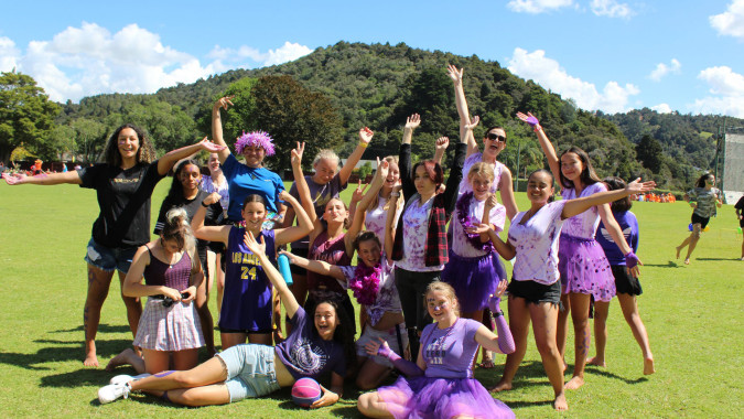 Eine Gruppe Schülerinnen der Whangarei Girls High School steht auf einer Wiese vor einer Berglandschaft.
