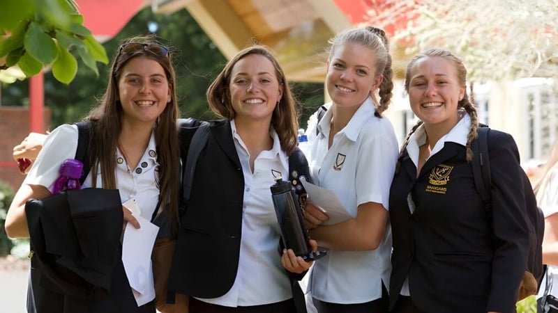 Vier Schülerinnen in Uniform stehen gemeinsam vor einem Backsteingebäude auf dem Campus der Whangarei Girls High School.