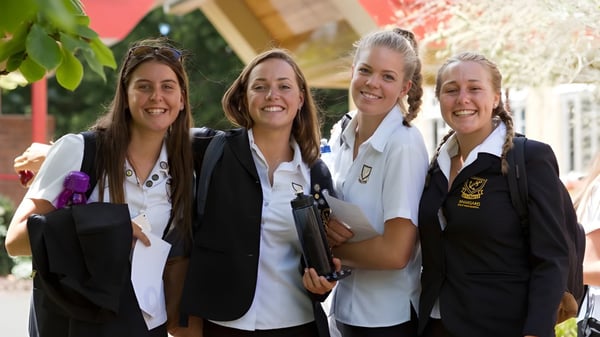 Vier Schülerinnen in Schuluniform stehen zusammen und lächeln auf dem Gelände der Whangarei Girls High School.