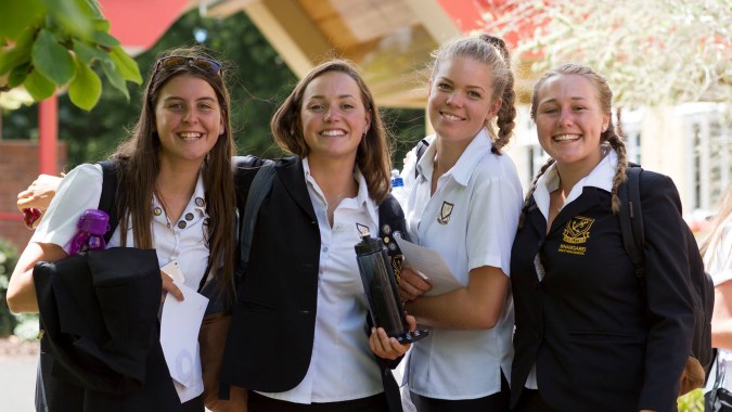 Vier Schülerinnen der Whangarei Girls High School stehen draußen vor einer Backsteinmauer und Grünfläche und lächeln zusammen.