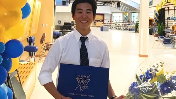 Ein lächelnder Schüler der Whistler Secondary School steht im bunten Flur mit Luftballons und hält eine blaue Mappe.