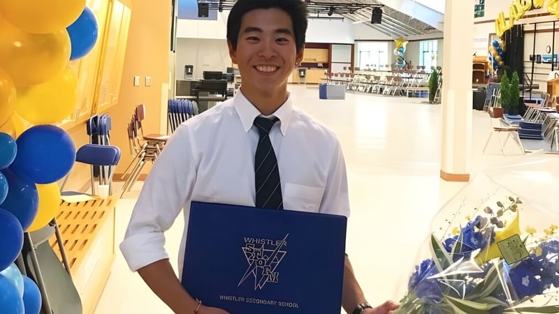 Ein lächelnder Schüler der Whistler Secondary School steht im bunten Flur mit Luftballons und hält eine blaue Mappe.