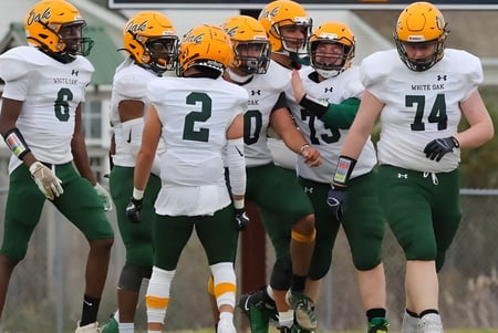 Eine Gruppe von Fußballspielern in grünen und weißen Trikots steht vor einem Gebäude auf dem Gelände der White Oaks Secondary School.