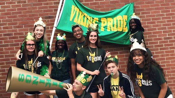 Eine Gruppe von Schülerinnen und Schülern der White Oaks Secondary School steht vor einer Backsteinmauer und hält eine grüne Flagge mit der Aufschrift MAINE PRIDE.