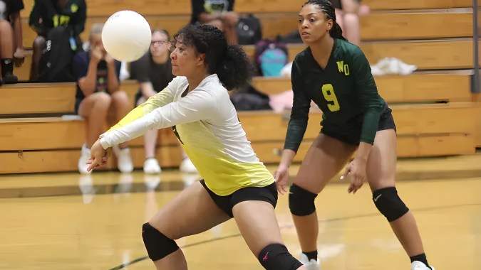 Zwei Volleyballspielerinnen der White Oaks Secondary School spielen in der Turnhalle ein Spiel mit Zuschauern im Hintergrund.