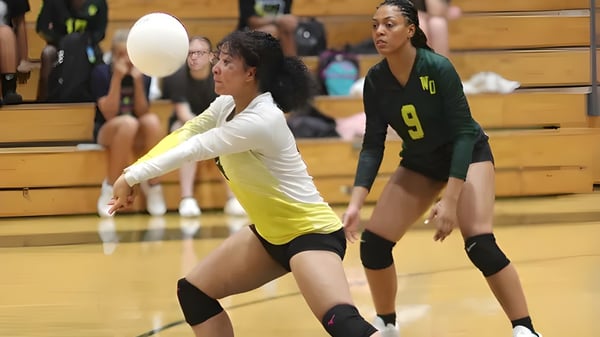 Zwei weibliche Volleyballspielerinnen der White Oaks Secondary School spielen auf dem Volleyballfeld mit Holzbänken im Hintergrund.
