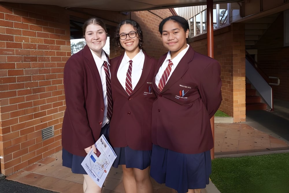 Drei Schülerinnen und Schüler des Whites Hill State College stehen zusammen im Flur und halten ein Schild.