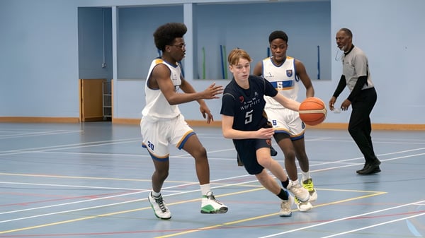 Eine Gruppe von Schülerinnen und Schülern der Whitgift School spielt Basketball auf dem Basketballfeld mit blauem Boden.