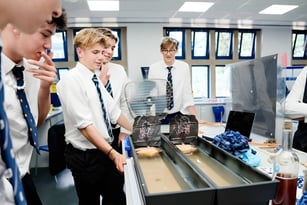 Eine Gruppe von Schülern der Whitgift School versammelt sich um einen Tisch mit verschiedenen Materialien im Schulgebäude.
