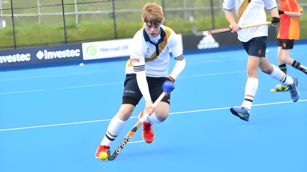 Ein Schüler der Whitgift School spielt auf dem blauen Kunstrasenfeld Feldhockey mit weiteren Spielern im Hintergrund.