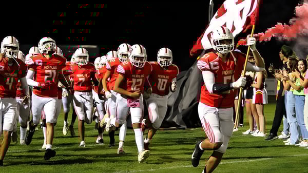 Fußballspieler der Whittier Christian High School rennen gemeinsam auf das Spielfeld während Cheerleader und Zuschauer im Hintergrund zu sehen sind.