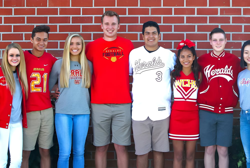 Eine Gruppe Schüler der Whittier Christian High School steht vor einer roten Ziegelwand in verschiedenen Sporttrikots und Freizeitkleidung.