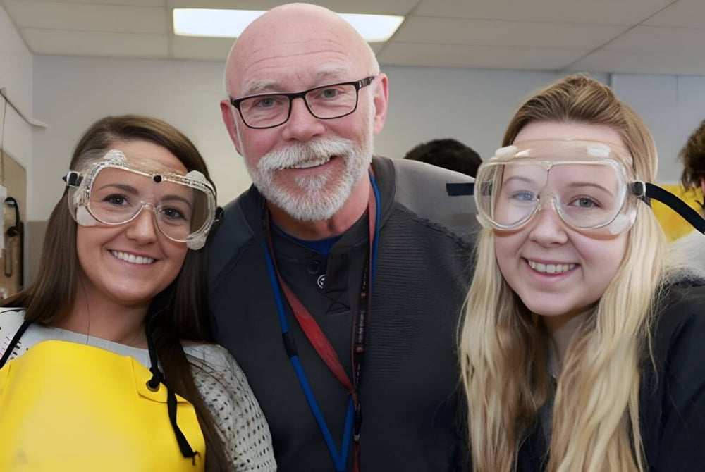 Drei Personen, zwei Frauen und ein Mann, stehen in einem Flur der William Aberhart High School und posieren für ein Gruppenbild.