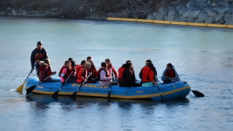 Schüler der William Aberhart High School sitzen in roten und orangen Rettungswesten auf einem blauen Schlauchboot auf dem Wasser.