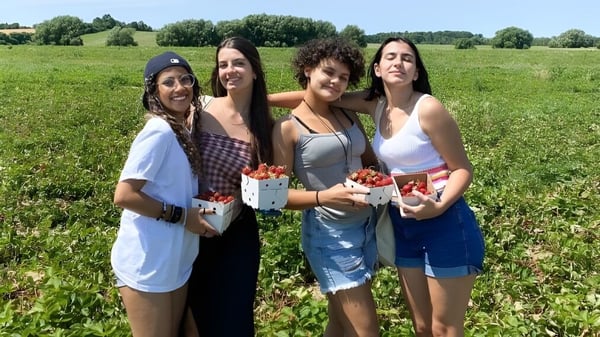 Vier Schülerinnen der William Academy stehen auf einem Feld und halten Körbe mit frischen Erdbeeren.