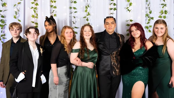 Eine Gruppe von Schülerinnen und Schülern in formeller Kleidung steht vor einem begrünten Hintergrund auf dem Campus des William Colenso College.