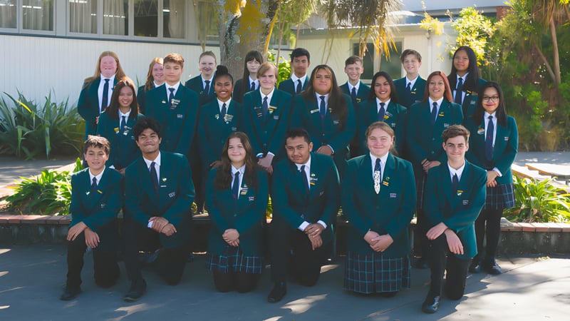 Eine Gruppe Schülerinnen und Schüler steht im Freien auf dem Campus des William Colenso College vor Bäumen und Gebäuden.