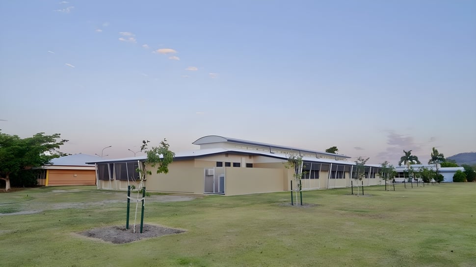 Das moderne Gebäude mit geschwungenem Dach auf dem Gelände der William Ross State High School vor einem grasbewachsenen Feld mit neuen Bäumen.