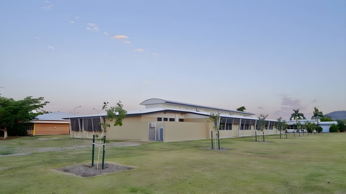 Das moderne Gebäude mit geschwungenem Dach auf dem Gelände der William Ross State High School vor einem grasbewachsenen Feld mit neuen Bäumen.