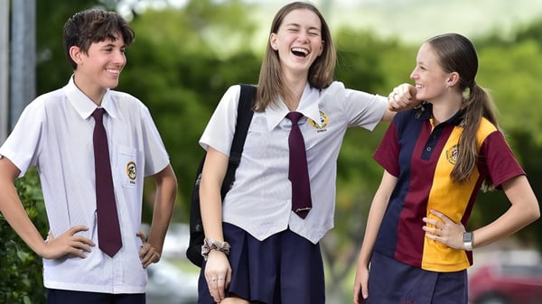 Drei Schüler der William Ross State High School unterhalten sich lachend im Freien vor grünem Hintergrund.